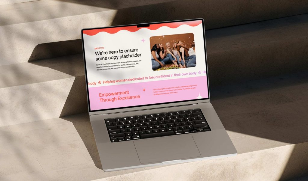 A laptop on a concrete surface displays a website with text "We're here to ensure some copy placeholder" and women.