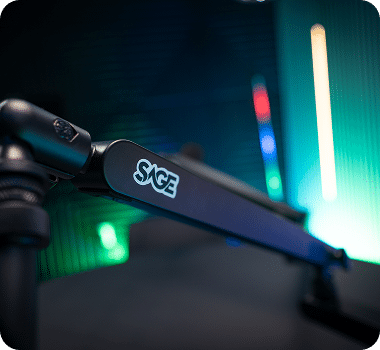 A black monitor arm with "SAGE" in white text extends across a blurred background with green and blue lights.