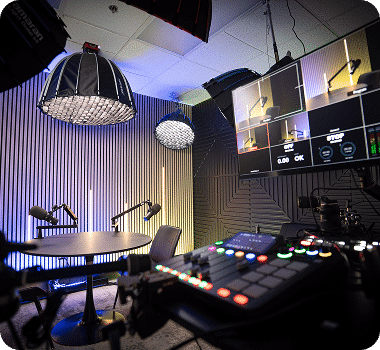 A professional podcast studio with sound-dampening walls, microphones, lighting, and a multi-screen monitor displaying "STOP".