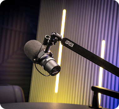 A black microphone on a boom arm with "SAGE" written on it, in a studio with yellow and purple lights.