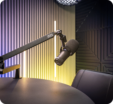 A black microphone on an adjustable arm extends over a dark table in a modern recording studio.