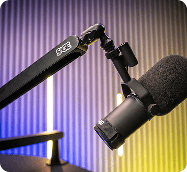 A black "SAGE" boom arm extends to a black microphone with a foam cover, against a purple and yellow lit wall.