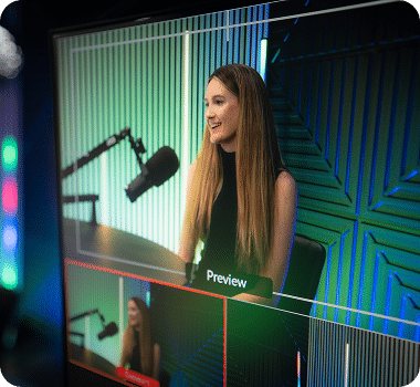 A woman with long brown hair smiles, sitting in front of a microphone on a screen with "Preview" text.