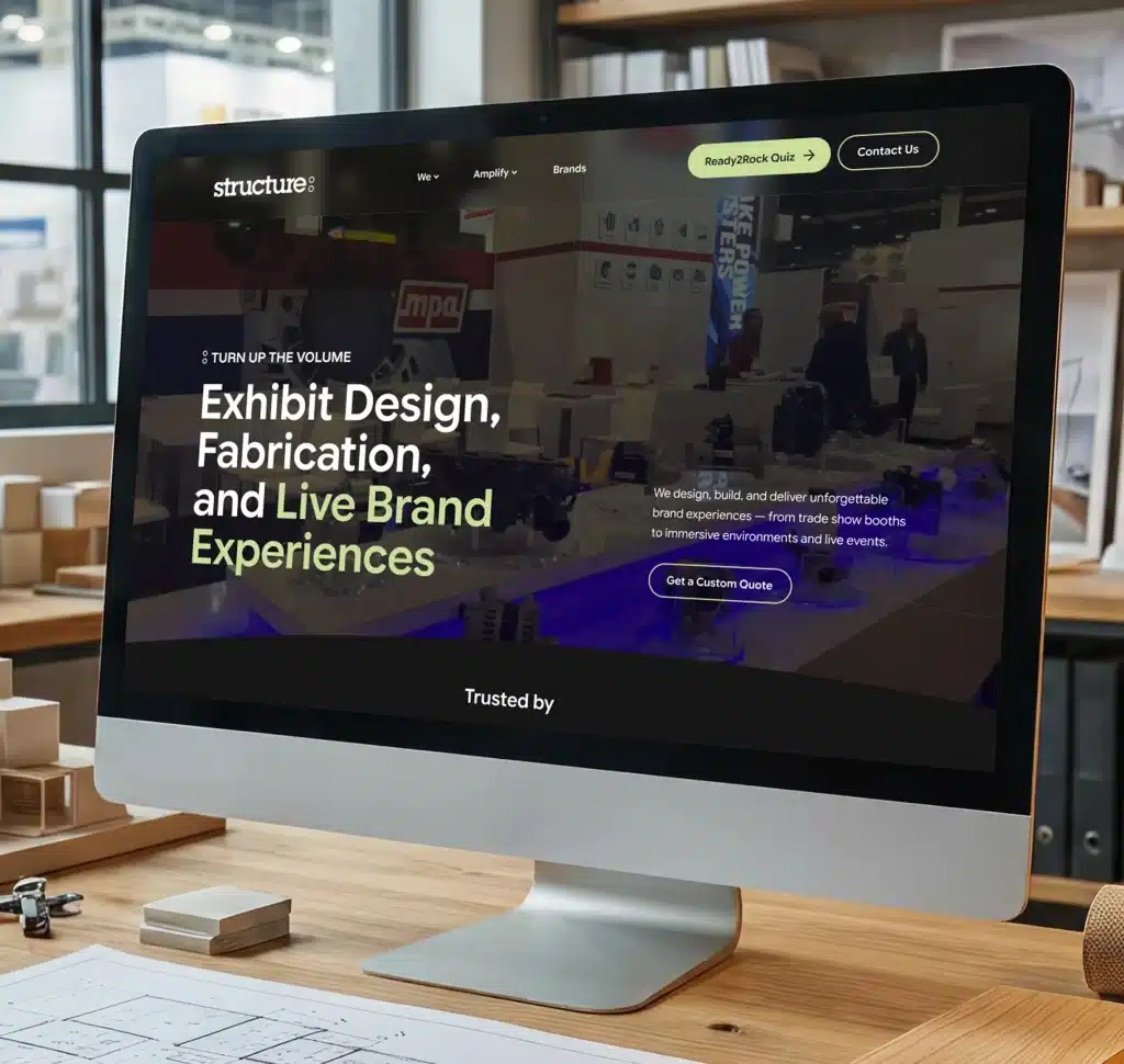 A computer monitor displays a website with the text "Exhibit Design, Fabrication, and Live Brand Experiences."