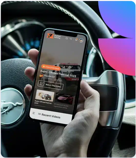 A hand holds a smartphone displaying "Super Offroad Festival 2023" over a car's steering wheel.