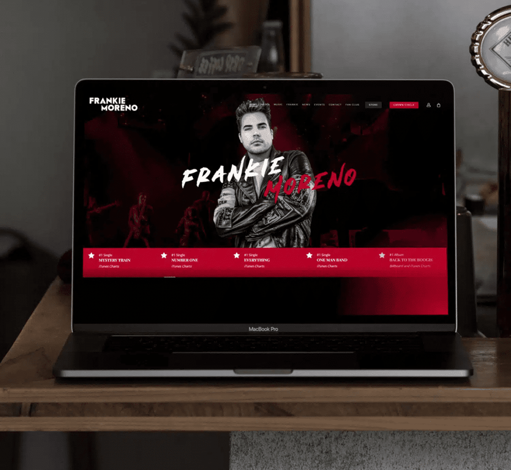 A MacBook Pro displays "FRANKIE MORENO" website with the artist in a leather jacket and red accents.
