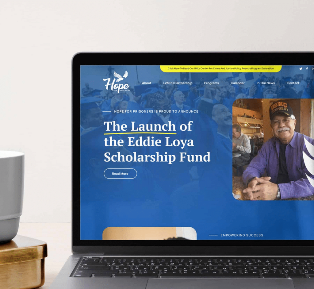 A laptop displays a website with "The Launch of the Eddie Loya Scholarship Fund" and a man in a "USMC" hat.