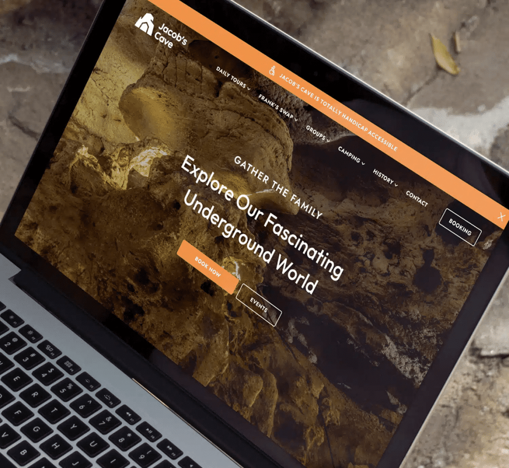 A laptop displays the "Jacob's Cave" website with text "Explore Our Fascinating Underground World" over a cave image.