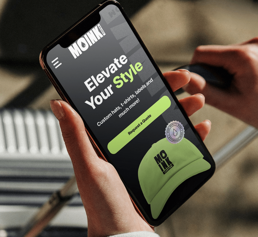 Hands hold a smartphone displaying "MOINK CUSTOM" and "Elevate Your Style" on a dark screen.