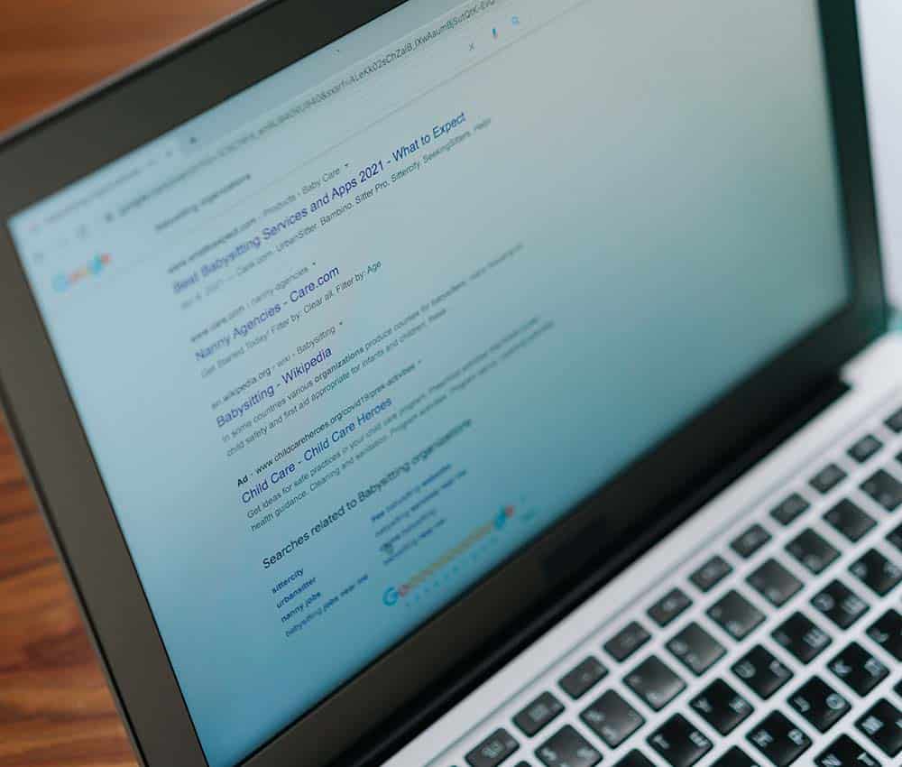 A laptop screen displays Google search results for "Babysitting Services and Apps 2021 - What to Expect."