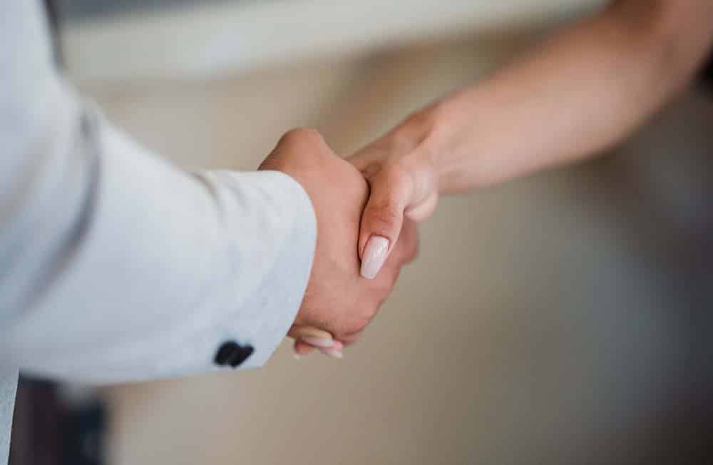 A man in a light suit jacket shakes hands with a woman whose nails are painted light pink.