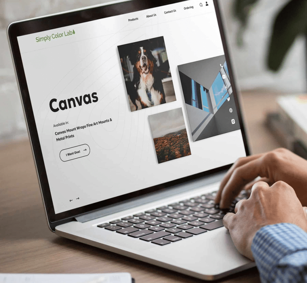 Hands type on a laptop displaying a website with "Simply Color Lab" and "Canvas" text, plus images of a dog and a landscape.