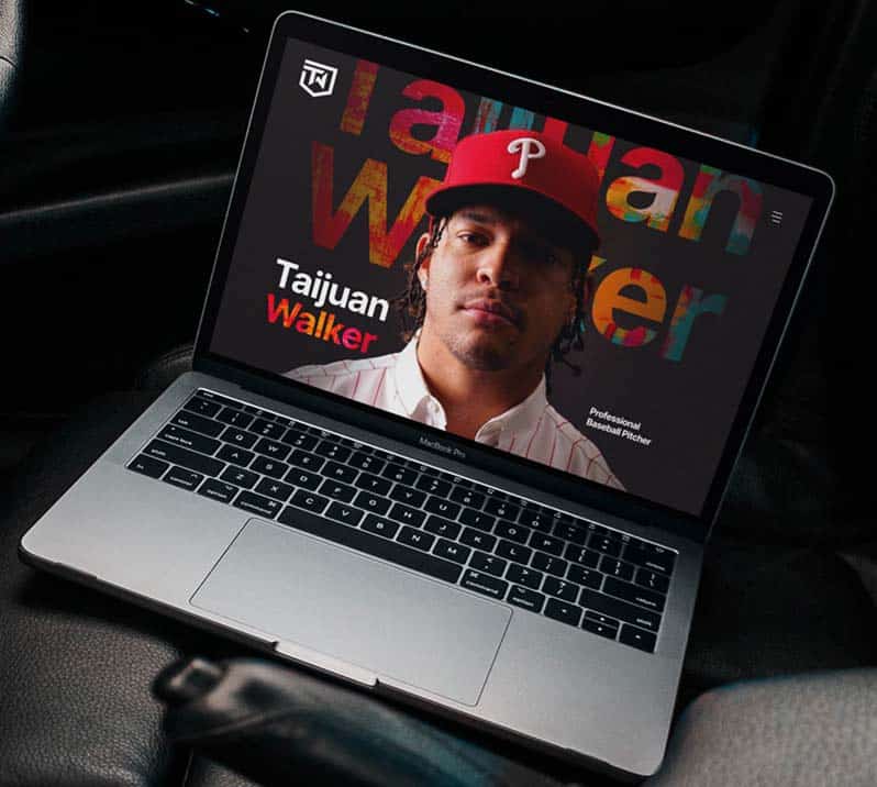 A MacBook Pro displays a website with "Taijuan Walker Professional Baseball Pitcher" and a man in a red cap.